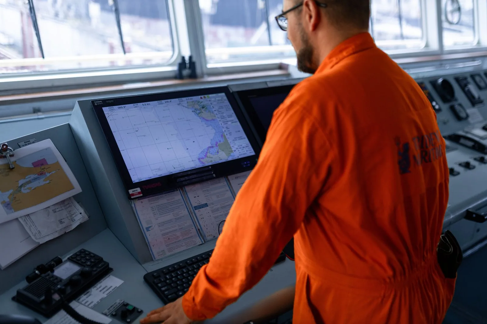 A bridge officer reviewing the voyage chart on the ship's navigation console — executing the voyage instructions agreed in the post-fixture phase.