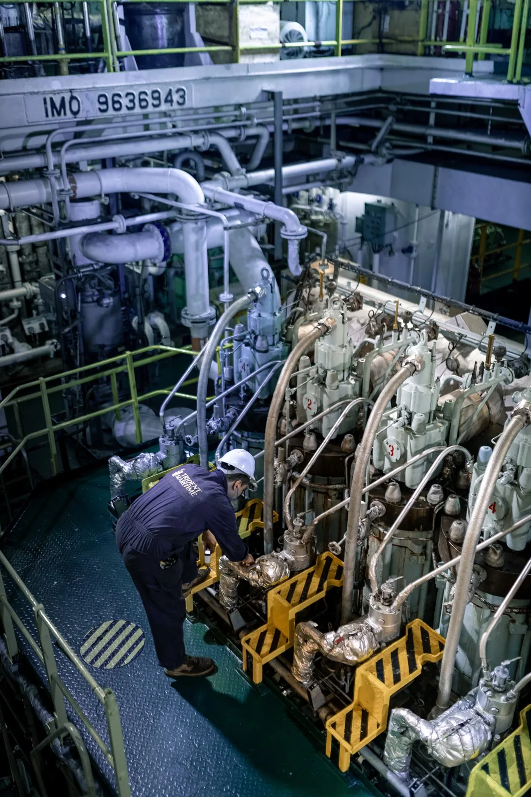 A crew member in a hard hat inspects a large marine engine during a pre-vetting inspection tanker check.