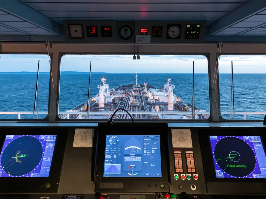 View from the bridge over a tanker's cargo deck, with ECDIS and radar displays in the foreground.