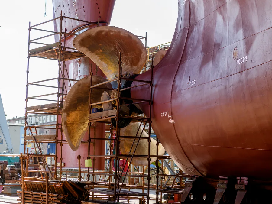 Propeller and stern of a vessel surrounded by scaffolding in dry dock.
