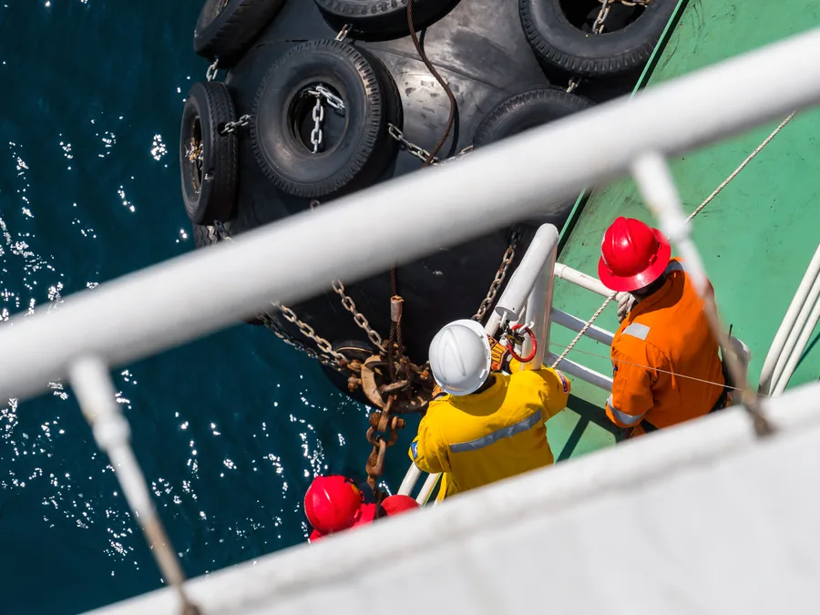 Crew in safety gear transferring to a vessel alongside fenders during an attendance.