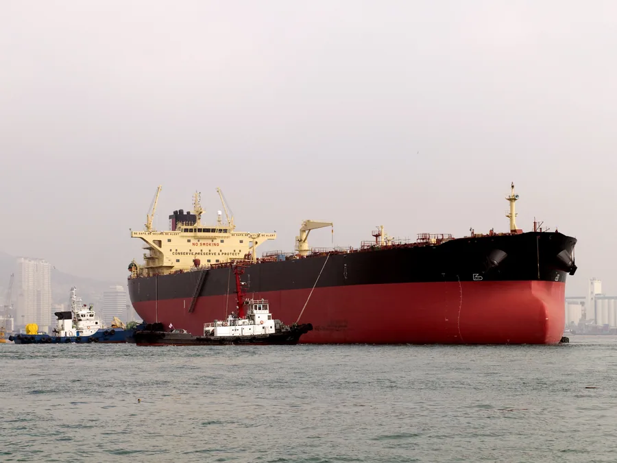 Laden crude oil tanker assisted by tugs on approach to port.